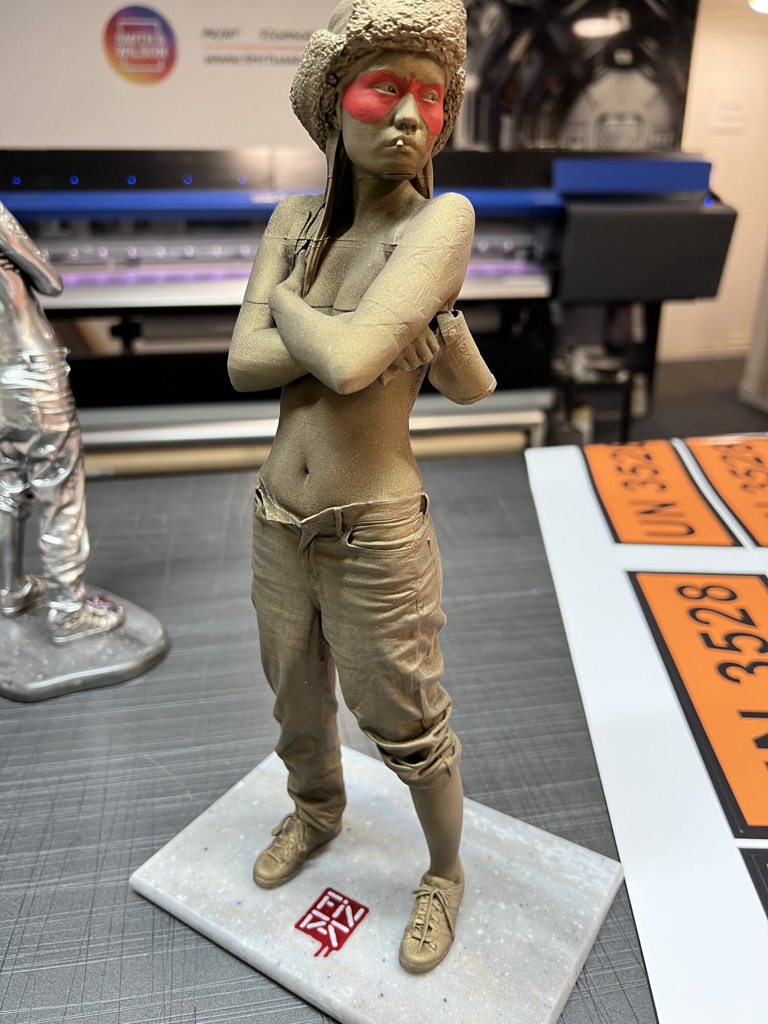 On the floor in front of the Mimaki UV printer — bronze edition staged next to the chrome.