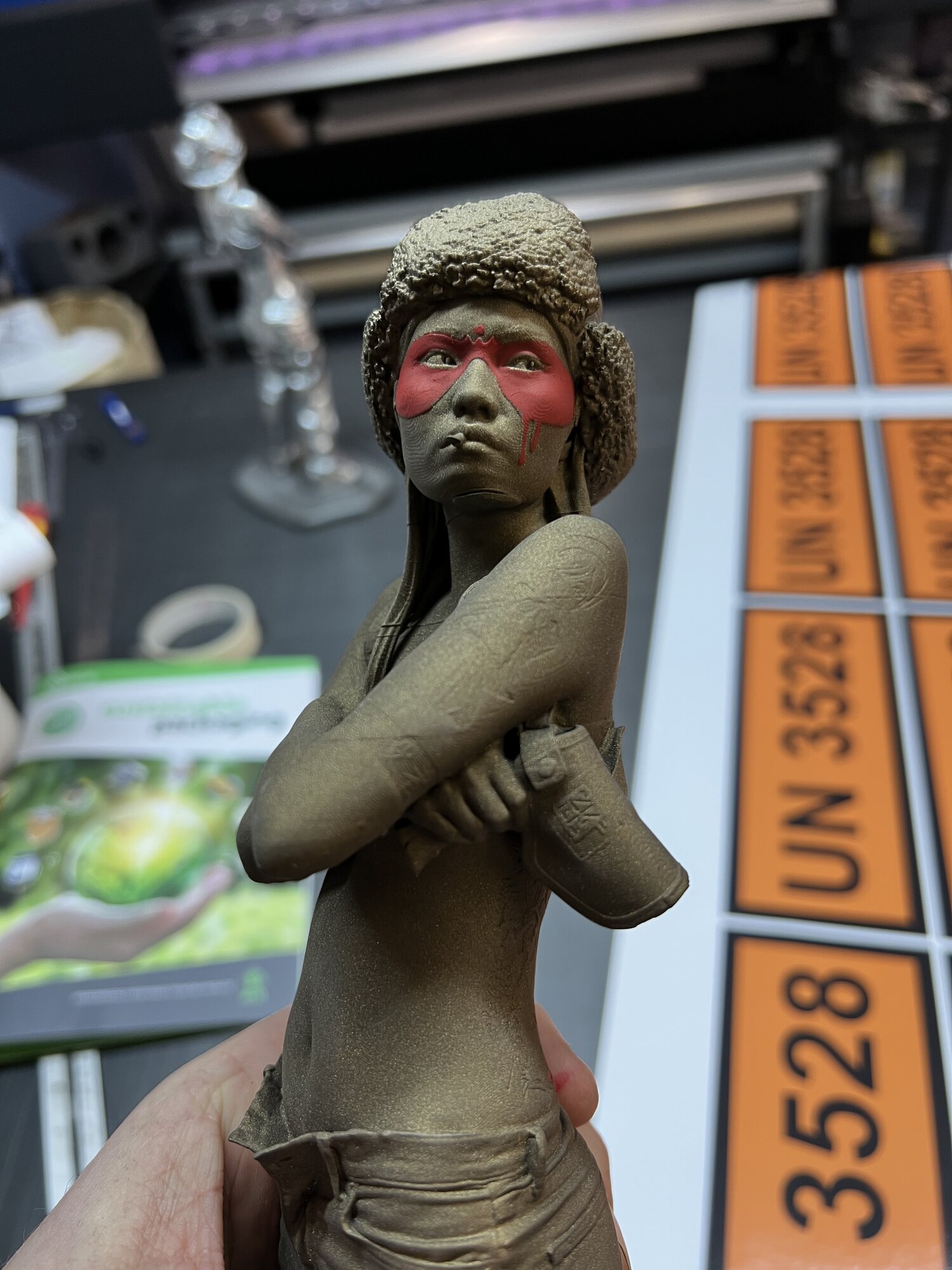 Face macro — hand-painted mask sitting on the matt bronze surface, sculpt detail held all the way through.